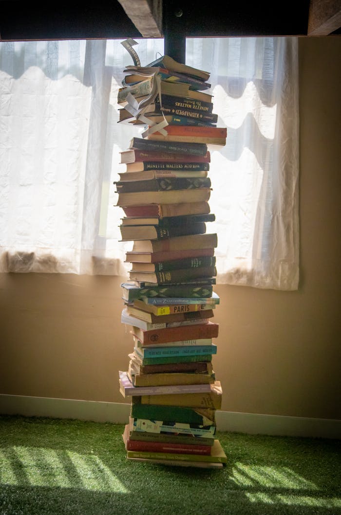 A tall stack of books casting a shadow near a sunlit window, indoors setting.